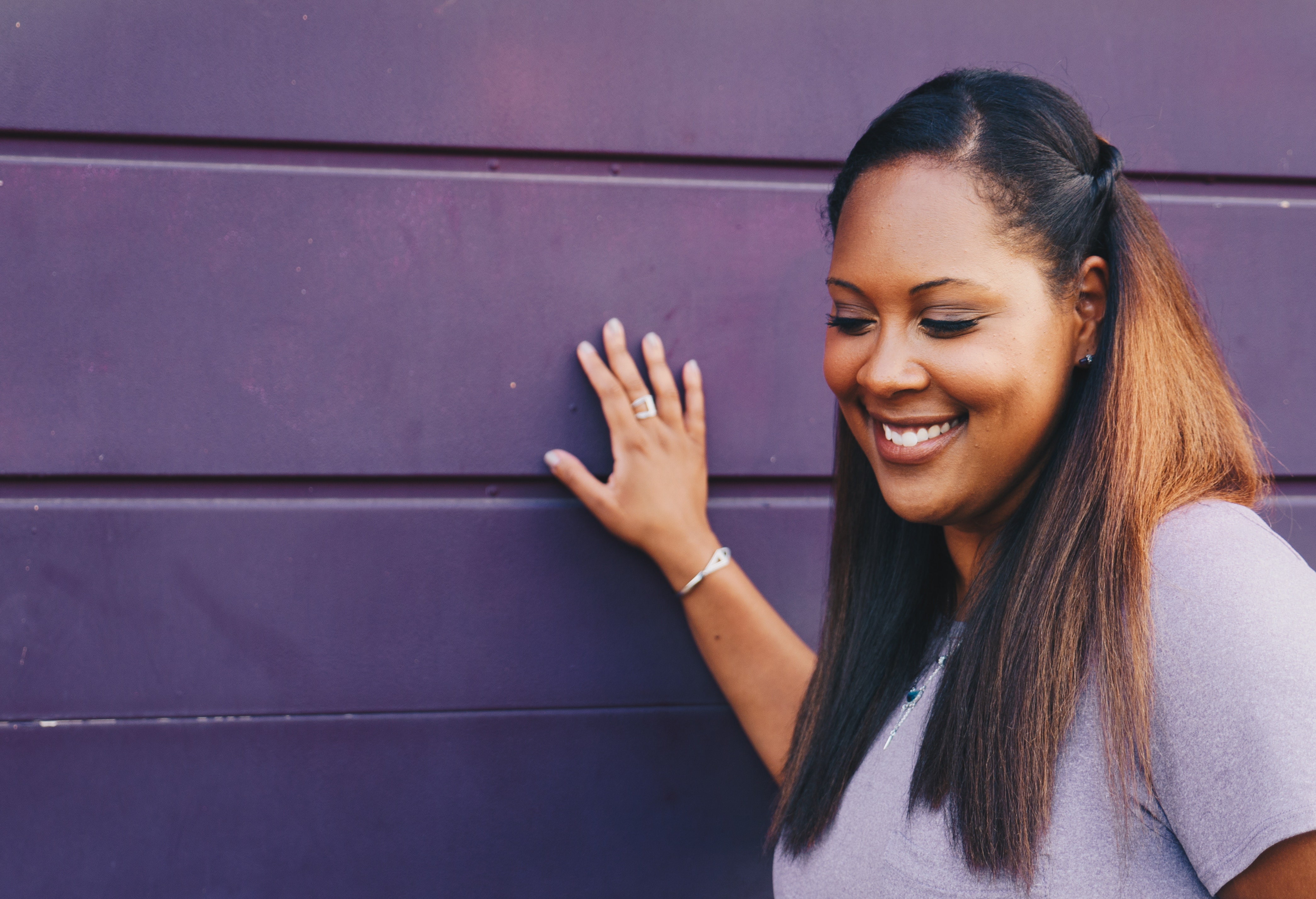 Girl by a purple wall with a simple half-up hairstyle.